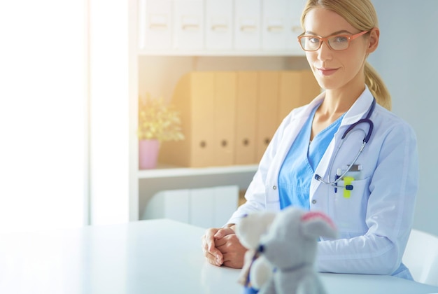 Bello giovane medico femminile sorridente che si siede allo scrittorio.