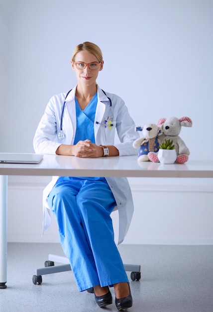 Bello giovane medico femminile sorridente che si siede allo scrittorio.