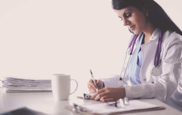 Bello giovane medico femminile sorridente che si siede allo scrittorio.