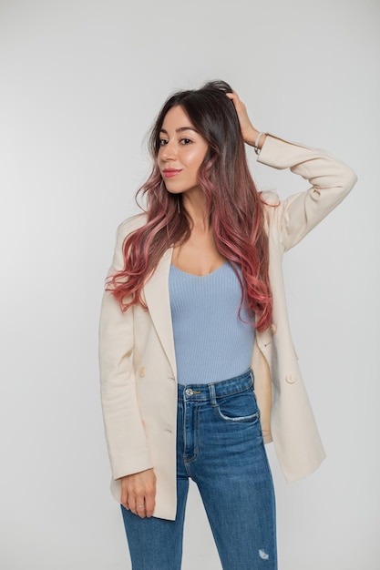 Bello giovane modello alla moda alla moda della donna con capelli rosa in un blazer superiore blu e jeans che posano su un fondo bianco