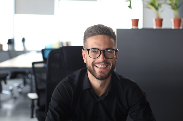 Bello giovane uomo d'affari che guarda l'obbiettivo mentre è seduto in ufficio.