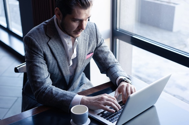 Bello giovane uomo in tuta completa utilizzando il computer mentre era seduto nella caffetteria