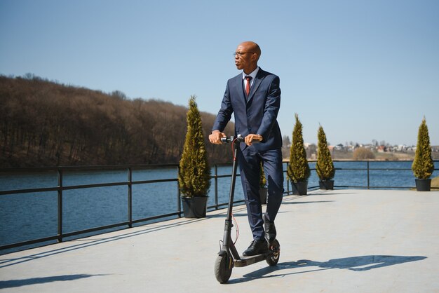 Bello imprenditore africano equitazione scooter elettrico all'aperto