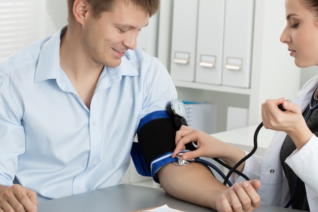 Bello medico femminile allegro della medicina che misura la pressione sanguigna al paziente. Concetto medico e sanitario