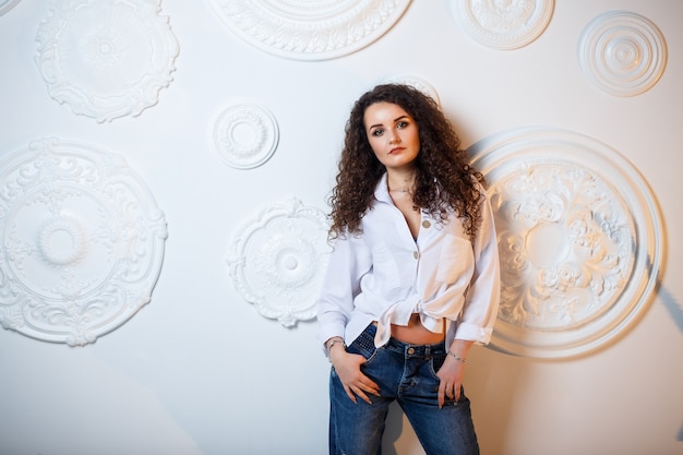 Bello modello della ragazza con la posa dei riccioli. Indossa una camicia bianca e jeans.