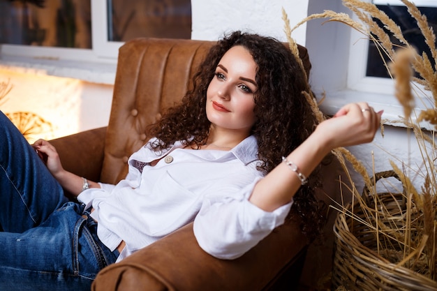 Bello modello della ragazza con la posa dei riccioli. Indossa una camicia bianca e jeans.