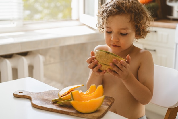 Bello ragazzino sveglio che mangia melone fresco.