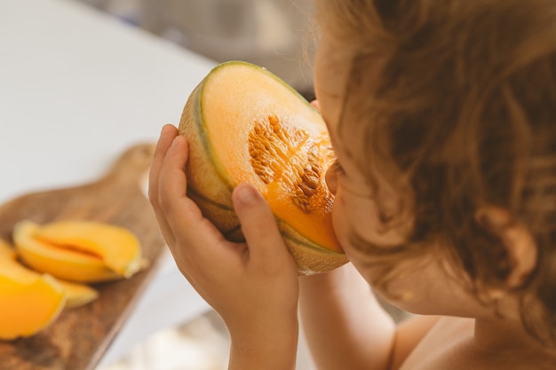 Bello ragazzino sveglio che mangia melone fresco.