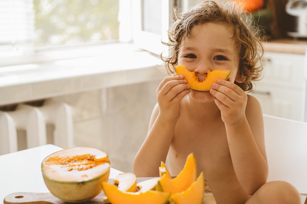 Bello ragazzino sveglio che mangia melone fresco.