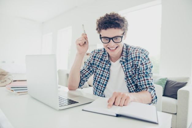 Bello ragazzo eccitato studente in bicchieri a casa fare il compito davanti al netbook