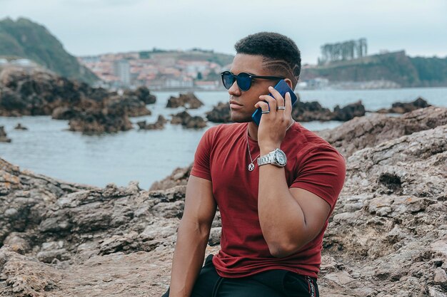 Bello scatto di un giovane con occhiali da sole che parla al telefono sulla spiaggia