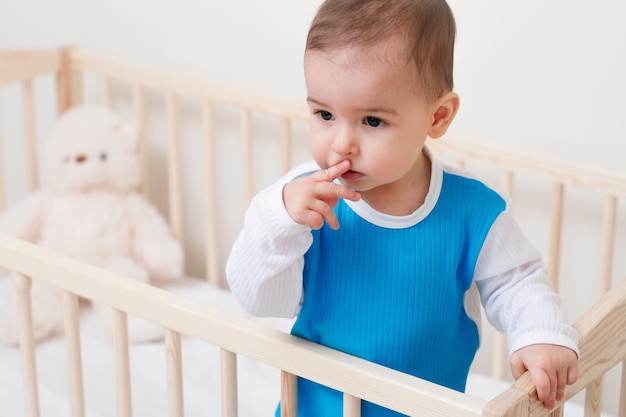 Bello sguardo adorabile del bambino del bambino da un lato con un orso e un dito sulla bocca nel letto su fondo bianco