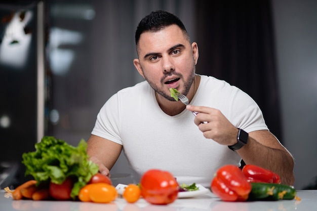 Bello uomo a mangiare cibo vegetariano sano a casa.