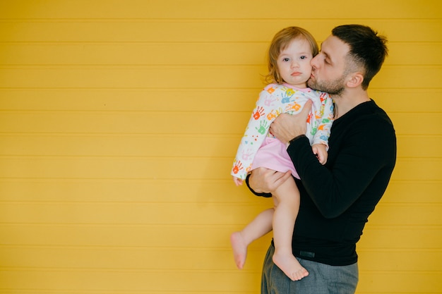 Bello uomo caucasico che tiene a disposizione la sua piccola figlia sopra la parete gialla