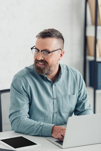 Bello uomo d'affari in camicia e occhiali utilizzando il computer portatile in ufficio