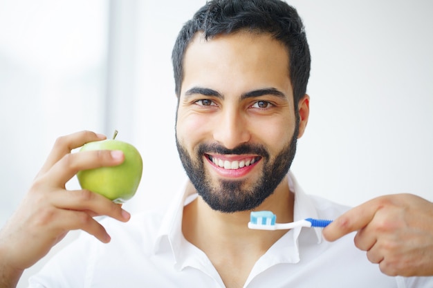 Bello uomo sorridente che pulisce i denti bianchi sani con la spazzola.