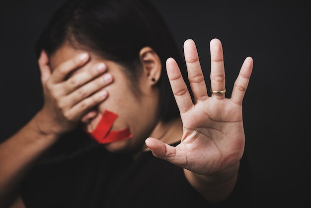 Benda della donna che avvolge la bocca con nastro adesivo rosso e mostra il segno della mano smettere di abusare della violenza