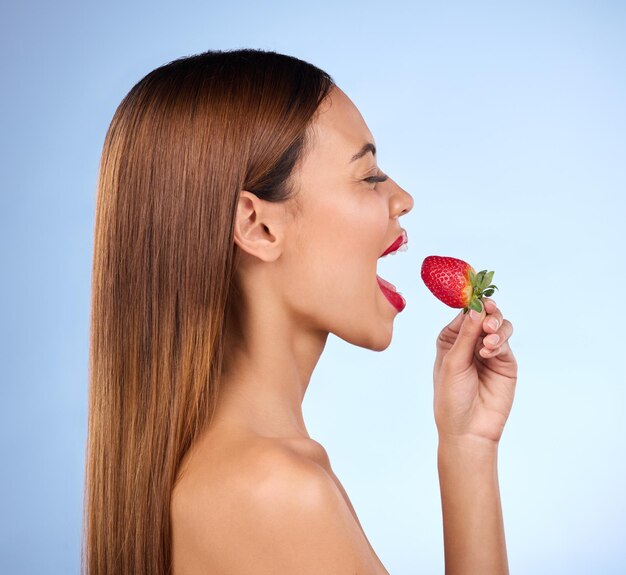 Benessere di bellezza e profilo di donna con fragola su sfondo blu per nutrizione dietetica e alimentazione sana Cura della pelle felice e ragazza con frutta in studio per trucco cosmetico e spuntino naturale