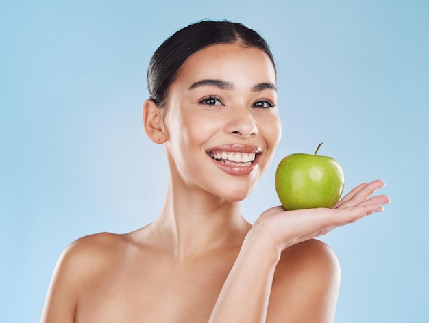 Benessere salute e bellezza con donna e una mela per nutrizione detox e dieta verde su sfondo blu Sorriso nutrizionista e frutta con femmina felice che mangia sano per uno stile di vita naturale