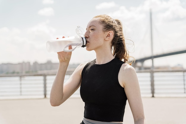 Bere acqua pulita da una bottiglia di plastica rompere il tempo una giovane donna felice allenamento all'aperto a cavallo