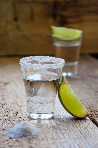 Bere alcol. Tequila d'argento con calce e sale sul tavolo di legno