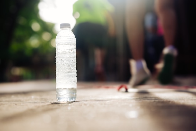 Bere bottiglia d&#39;acqua sul terreno e le persone sfocate si esercitano facendo jogging