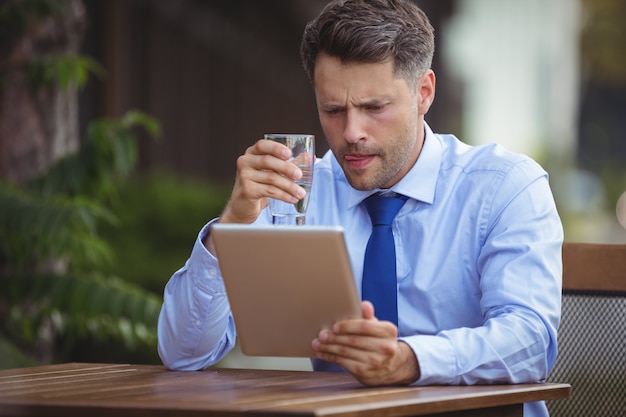 Bere dell'uomo d'affari mentre per mezzo della compressa digitale