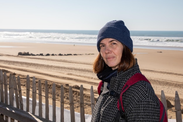 Berretto da donna con zaino che cammina sulla sabbia della costa della spiaggia in inverno