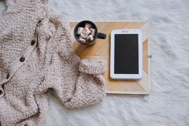 bevanda al cioccolato caldo, smartphone tablet con schermo vuoto e usura in maglia sul vassoio da portata in legno