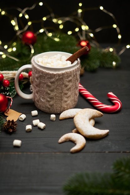 Bevanda calda al cacao con bastoncino di cannella e marshmallow con decorazioni natalizie sullo sfondo