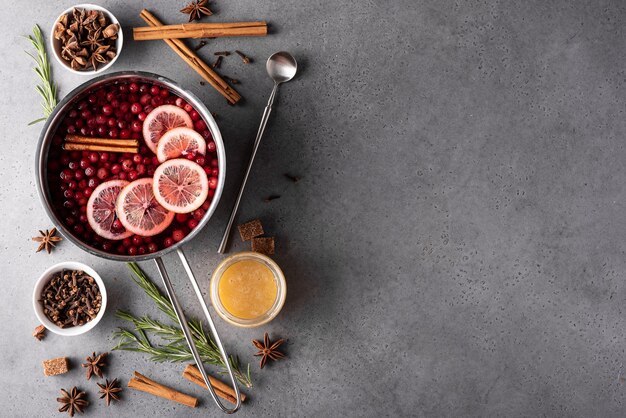 Bevanda calda al mirtillo rosso con miele di limone e spezie in una casseruola grigia, vista dall'alto