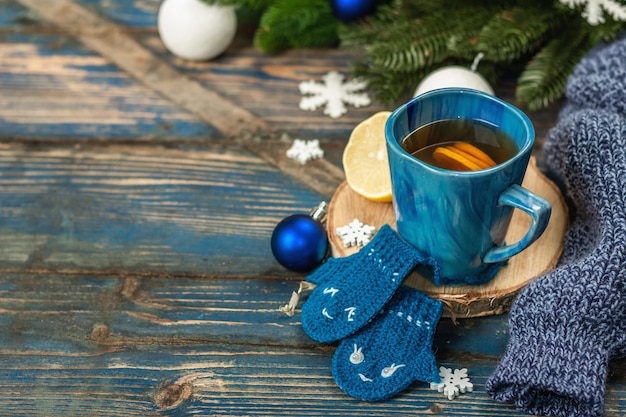 Bevanda calda con guanti divertenti all'uncinetto. Decorazioni invernali tradizionali, rami di abete, fiocchi di neve. Disposizione festiva stagionale nei toni del blu, vecchio sfondo di legno, spazio per la copia