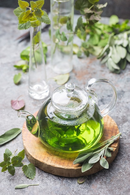 Bevanda calda di tè alla menta sedativo a base di erbe in una teiera di vetro su un vassoio di legno con menta fresca da giardino