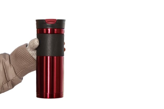 Bevanda calda nel thermos del bicchiere Thermos della tazza termica che tiene la mano della ragazza in guanti caldi a maglia su bianco