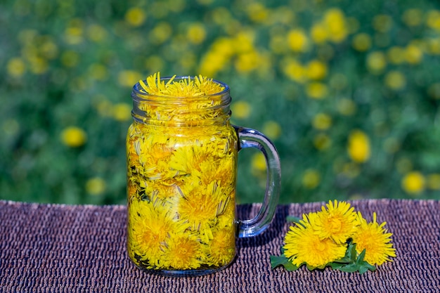 Bevanda del tè del fiore giallo del dente di leone in tazza di vetro sul tavolo, all'aperto