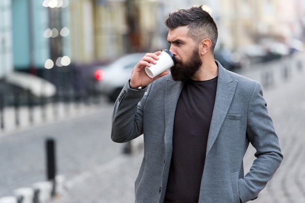 Bevanda deliziosa. Uomo barbuto hipster bere caffè tazza di carta. Uomo d'affari ben curato godersi la pausa caffè all'aperto sfondo urbano. Preferisci il caffè in viaggio. Riflessivo ma rilassato. Prenditi cura di te stesso.