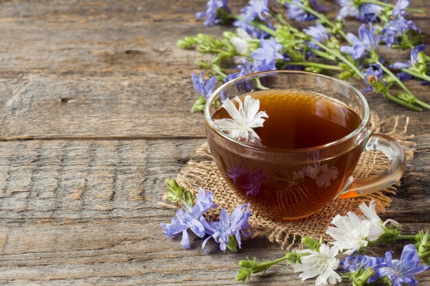 Bevanda della cicoria in tazza e fiori su fondo di legno rustico. Pianta medicinale Cichorii.