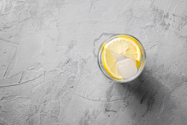 Bevanda di acqua ghiacciata fresca con limone in vetro su sfondo concreto, spazio di copia vista dall'alto