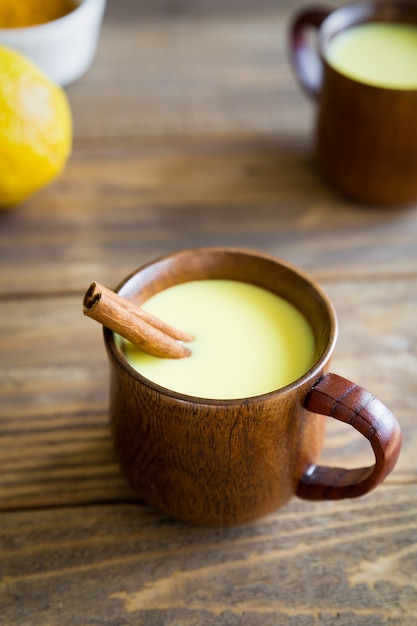 Bevanda di curcuma latte d'oro in una tazza di legno con un bastoncino di cannella si chiuda su un fondo di legno.