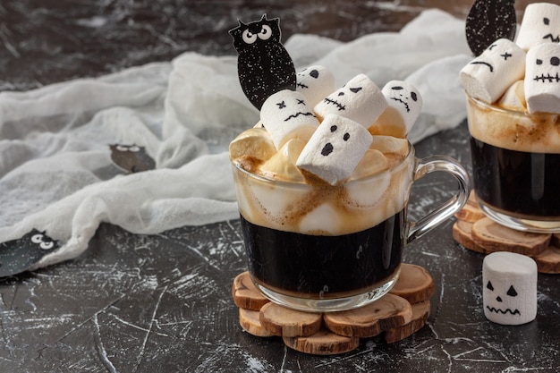 Bevanda di Halloween - due tazze di caffè con marshmallow (facce spettrali, mostro) sul tavolo scuro