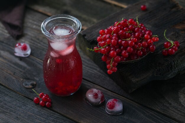 Bevanda estiva con spumante bianco. Cocktail di frutta rinfrescante fatto in casa o punch con champagne, ribes rosso, cubetti di ghiaccio e foglie di menta su un legno scuro