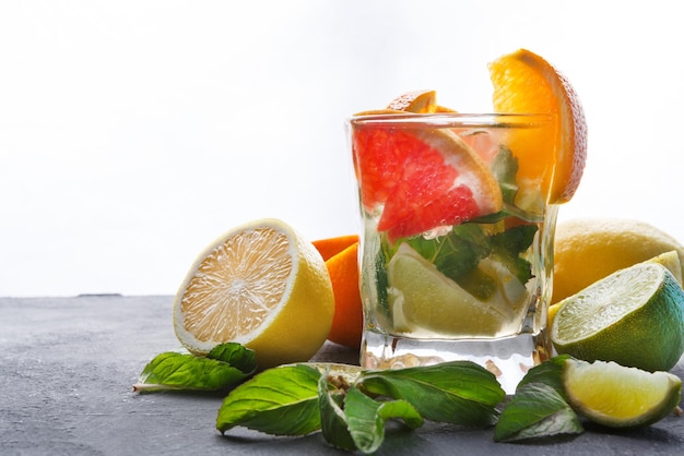 Bevanda estiva di agrumi a sfondo bianco. Acqua detox in vetro e varietà di frutta. Sfondo colorato con arance, limone e lime, copia spazio. Bevande da bar o concetto dietetico di alimentazione sana