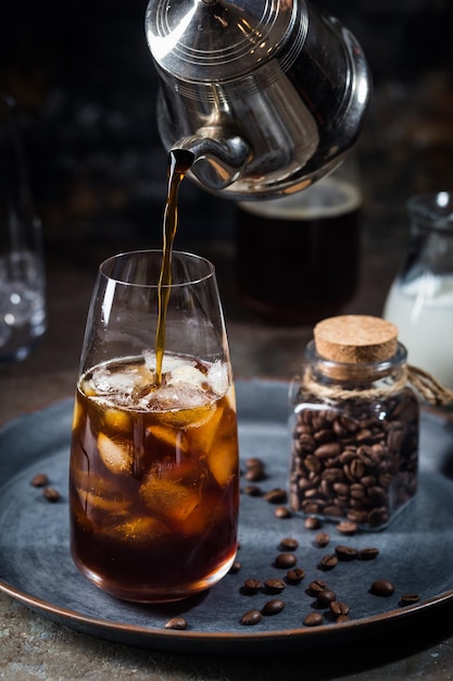 Bevanda estiva fredda di caffè freddo in un bicchiere alto con caffè e chicchi di caffè versati su uno sfondo di pietra.