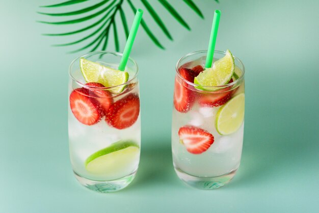 Bevanda estiva rinfrescante con lime e ghiaccio alla fragola in bicchieri su sfondo verde