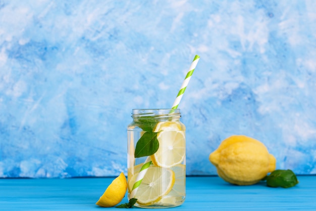 Bevanda gustosa con limone e basilico in barattolo di vetro su sfondo blu