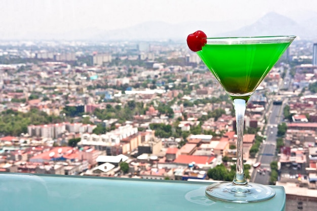 Bevanda Midori green Martini guarnita con ciliegia e vista panoramica sullo stile di vita della città