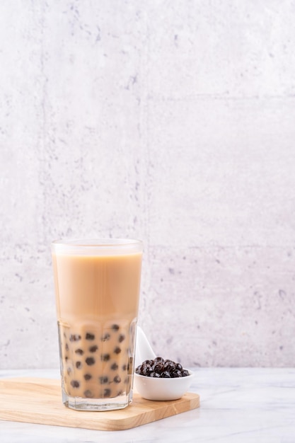 Bevanda popolare di Taiwan Tè al latte bollente con palla di perle di tapioca in bicchiere su tavola bianca in marmo vassoio di legno sfondo primo piano spazio per la copia