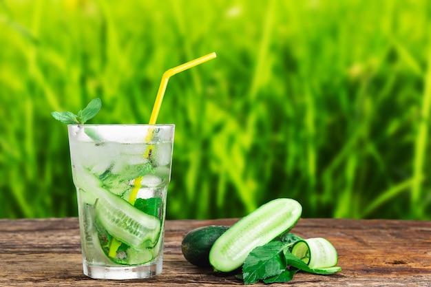 Bevanda rinfrescante con cetriolo e menta in un bicchiere con una cannuccia accanto a cubetti di ghiaccio contro un ba verde