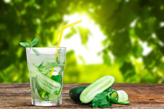 Bevanda rinfrescante con cetriolo e menta in un bicchiere con una cannuccia accanto a cubetti di ghiaccio su uno sfondo verde