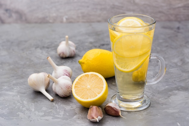 Bevanda terapeutica di limone e aglio in un bicchiere sul tavolo. Medicina alternativa, trattamento con rimedi popolari.